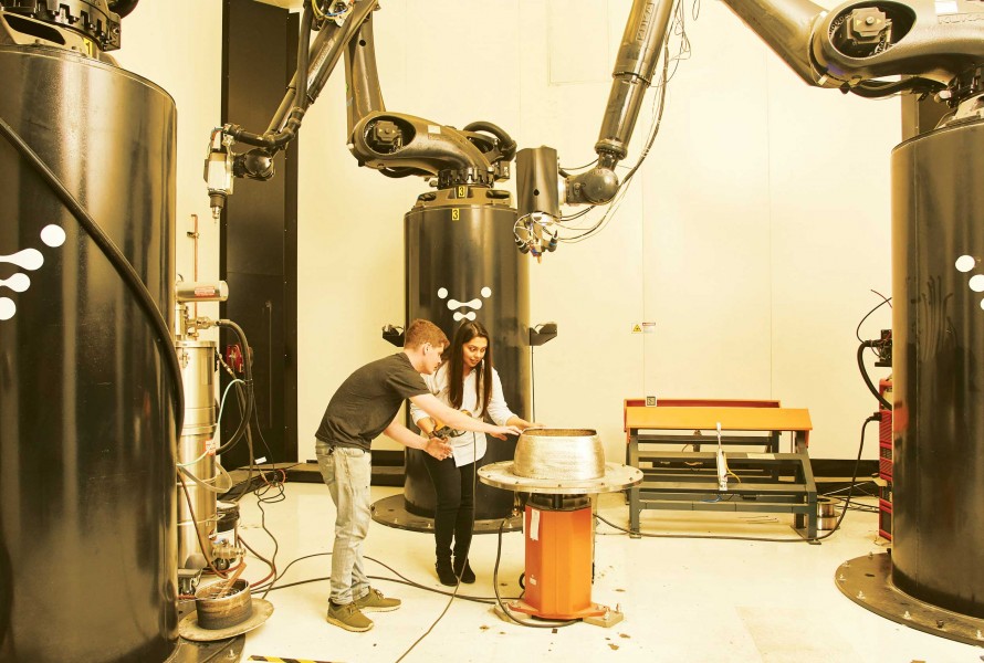 Two people working alongside 3D printer robot arms