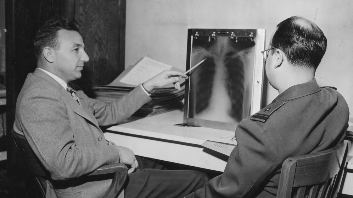 Black and white photo of two men looking at chest x-rays