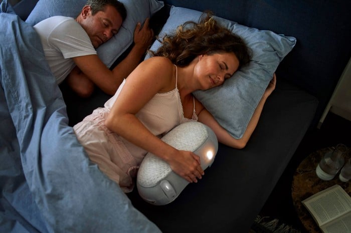 Photograph of a couple sleeping. Woman is holding the Somnox robot.