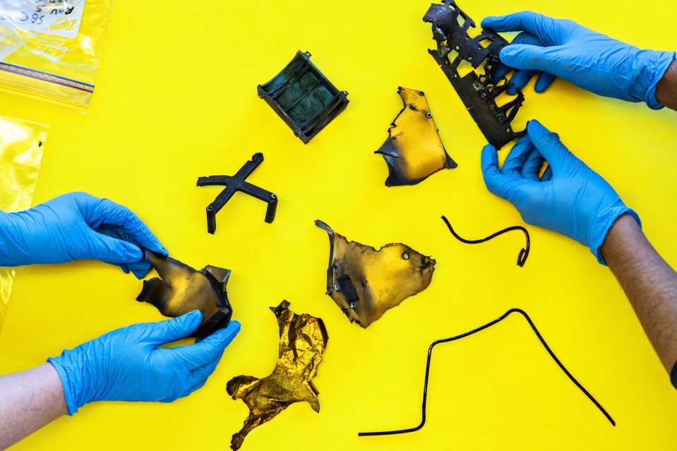 Photograph of two people wearing gloves examining space debris on a yellow table top