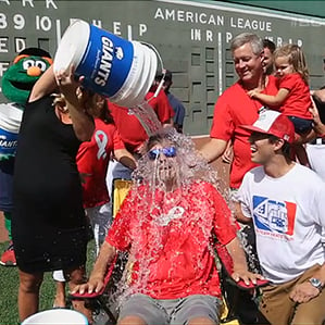 man getting cooler of ice water poured over his head with onlookers