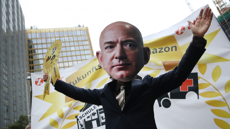 A person wearing a giant Jeff Bezos mask stands in front of a protest.