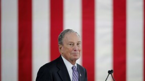 Michael Bloomberg, during a speaking event, with the stripes of the American flag in the background.