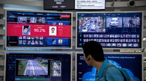 A man walks in front of screens showing facial recognition systems in action