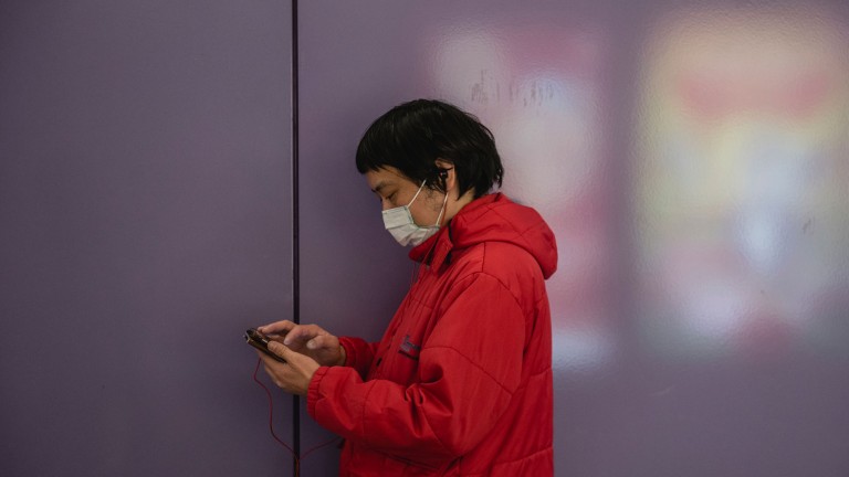 A man in Hong Kong in a face mask checks his phone