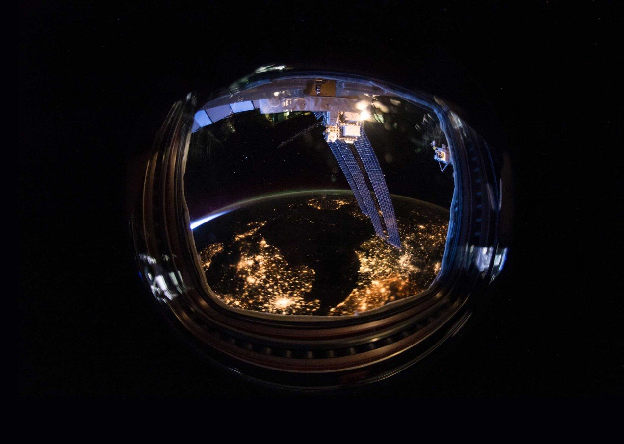 An astronaut helmet reflecting a light-filled earth
