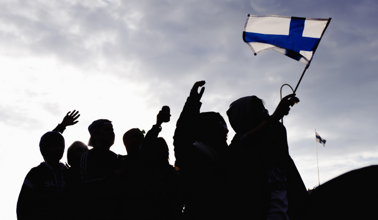 Silhouettes of people raising Finland's flag.