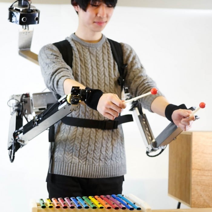 Image of man playing the xylophone wearing robotic-armed backpack.