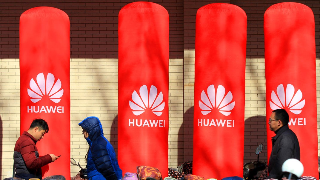 Pedestrians walk past an advertisement for Huawei