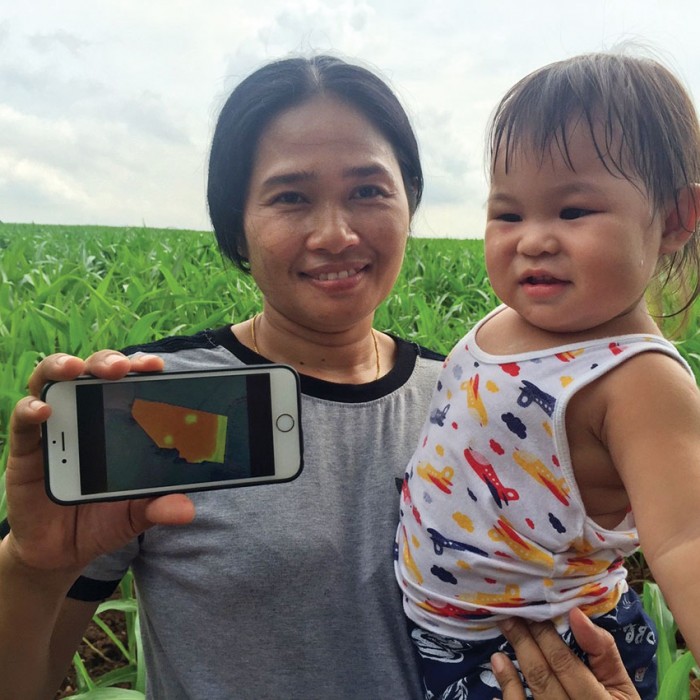 Photo of a farmer in Thailand, holding up an iPhone showing a digital map.