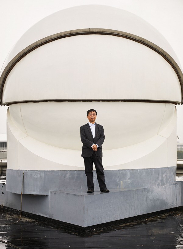 Photograph of Jian-Wei Pan, standing in front of a receiver used in the transmission of ultra-­secure signals from the Micius satellite, has helped lead China’s quantum efforts. The picture of the receiver on the previous page shows a spotting laser used to help the satellite connect to the ground station.