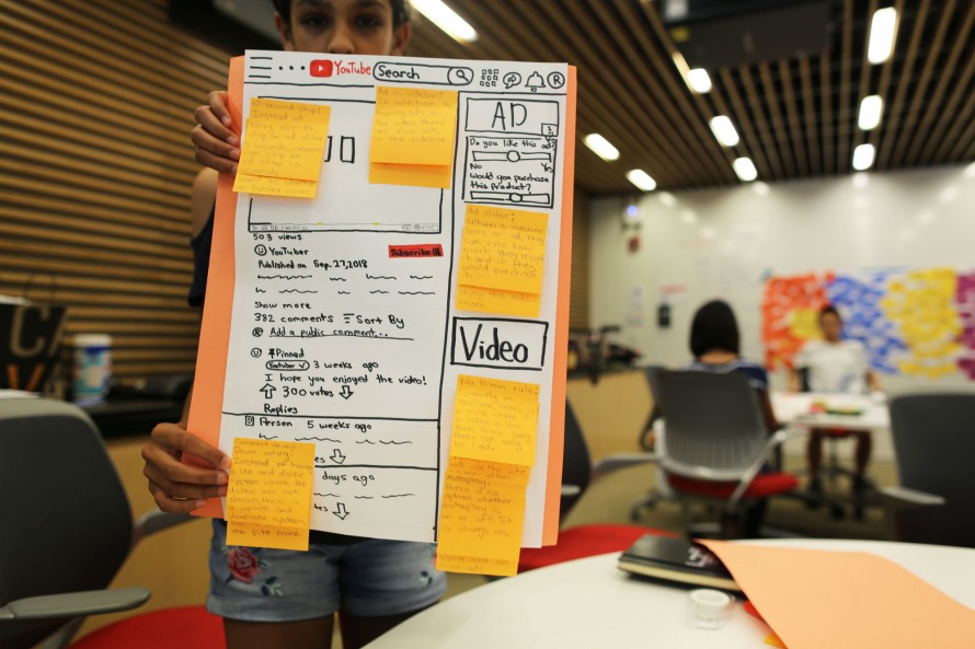 A student holds up a poster design of a hand-drawn YouTube web interface