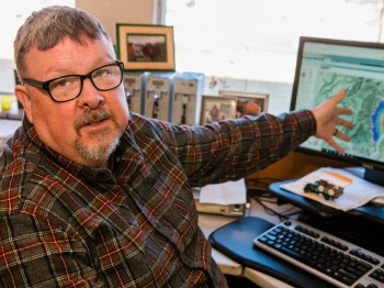 Photograph of Chuck as he works in his office at the Missoula Fire Lab and uses a program that models fire activity and the probability of spread. The program allows scientists to model fire spread and subsequently determine if action needs to be taken or what action they should be thinking about. Or, conversely, no action at all.