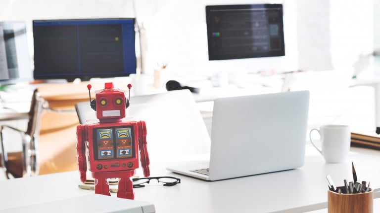 Image of a toy robot sitting on a desk next to a computer.