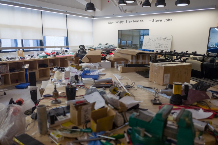 Photograph of a messy maker space with a quote from Steve Jobs on the wall that reads "Stay hungry, stay foolish"