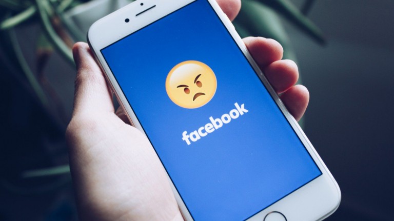 A phone with Facebook's app open, masked by an angry emoji