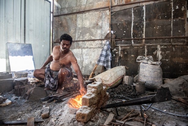 Photograph of Sidhappa Ji, a blacksmith who is using a solar-powered blower to stoke his fire
