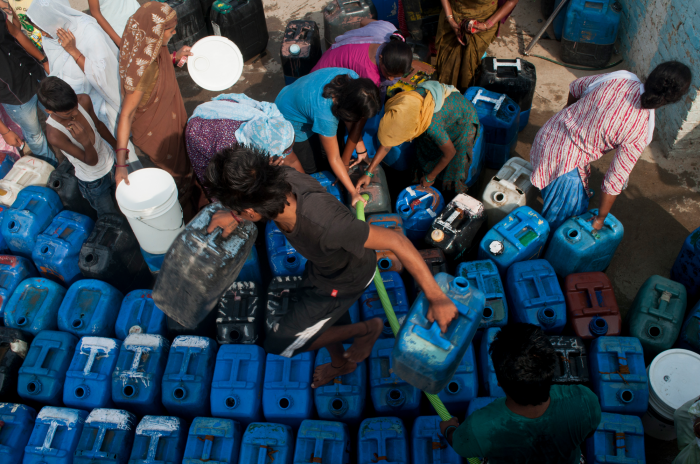 Image of a group of people trying to fill up blue water jugs with clean water