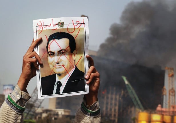 Photo of a protestor in Tahrir Square holding a photo showing President Mubarak's face crossed out
