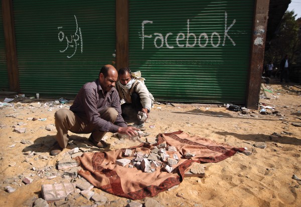 Photo of two men breaking paving stones in Cairo, Egypt in front of a building with "facebook" spray-painted on it