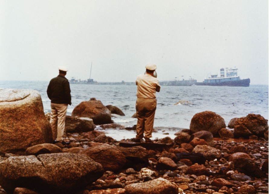 Image from 1969 showing US Coast Guard officers facing the ocean and oil barge Florida.