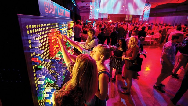 Photo of two people using a large Lite-Brite board in the forefront of a social gathering
