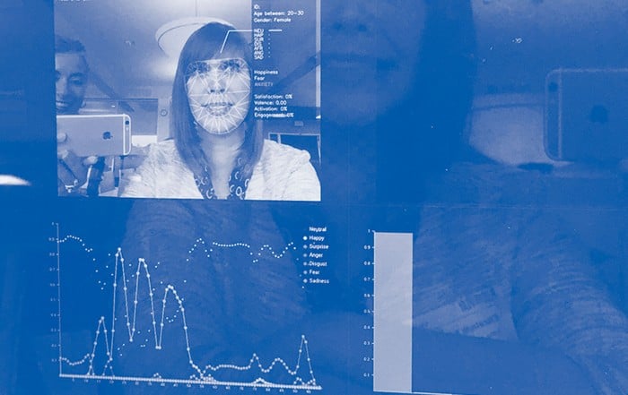 Photo of a computer screen. Windows on the screen show a graph and woman's face under facial recognition markers.