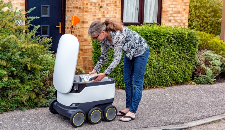 A woman taking a package out of a delivery robot