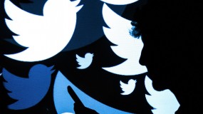 A silhouette of a man standing in front of a screen with Twitter logos on it