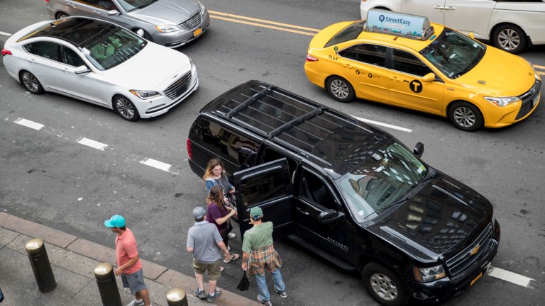 Traffic surrounds a ride-hailing taxi picking up passengers in New York
