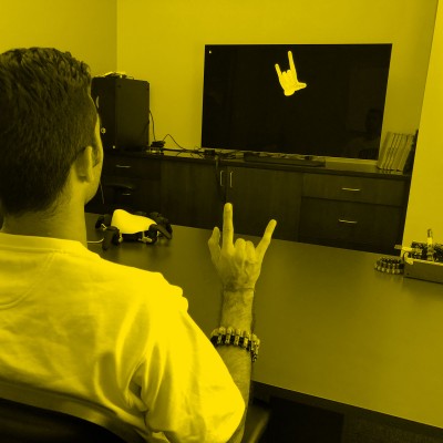 Image of person wearing wristband, making a hand gesture, and gesture appearing on a television screen